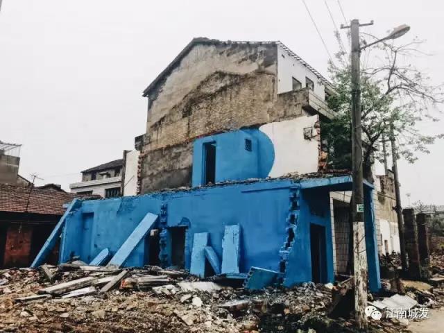 △ 這棟建筑是臨江最近的半拆遷建筑物的遺留，沅江和堤壩成為了展覽的天然背景。創(chuàng)作團(tuán)隊(duì)對(duì)這棟建筑進(jìn)行了半涂裝，將符號(hào)性的沅水曲線與拆遷進(jìn)行中的建筑立面進(jìn)行意義的疊造，它們共同觸發(fā)了場(chǎng)所空間多元語境的生成，把拆遷這種暫時(shí)破壞性、干擾性的介入行動(dòng)與沅水右岸發(fā)展的未來性、美好性緊密融合。